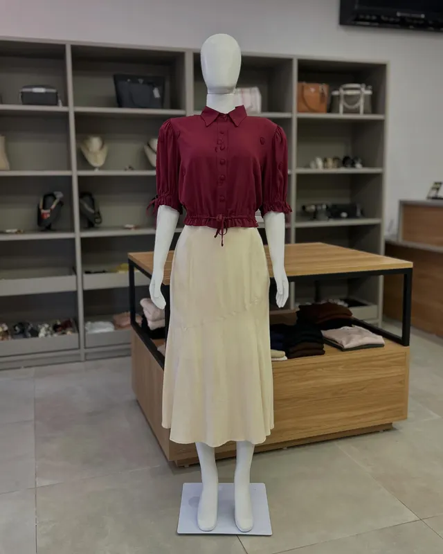 Camisa vinho de manga bufante com saia midi bege, no manequim, dentro da loja