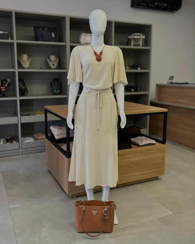 Conjunto creme de blusa e saia midi, no manequim, dentro da loja
