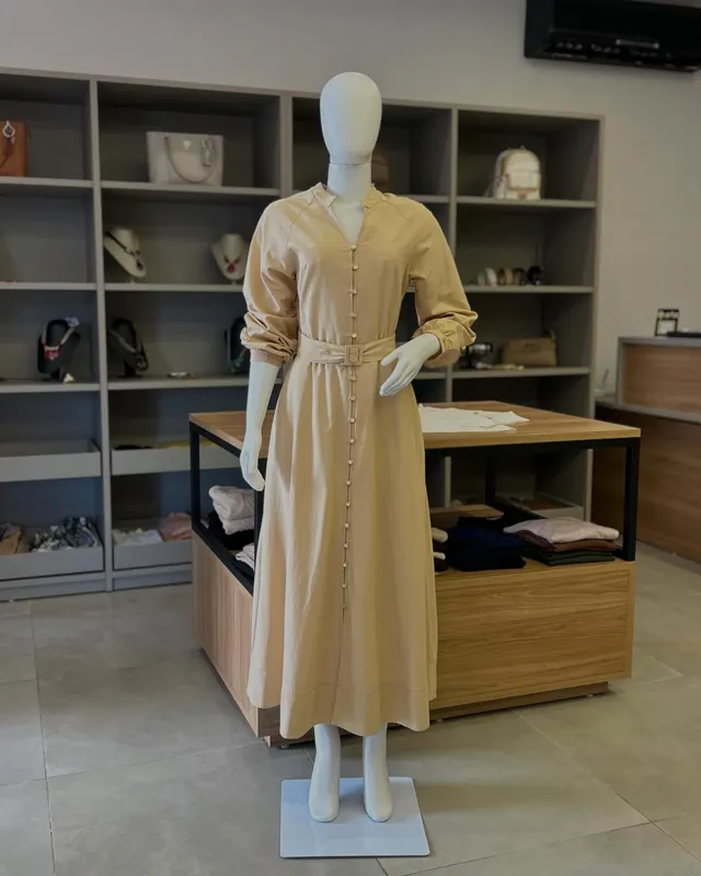 Vestido longo dourado de botões com cinto, no manequim, dentro da loja