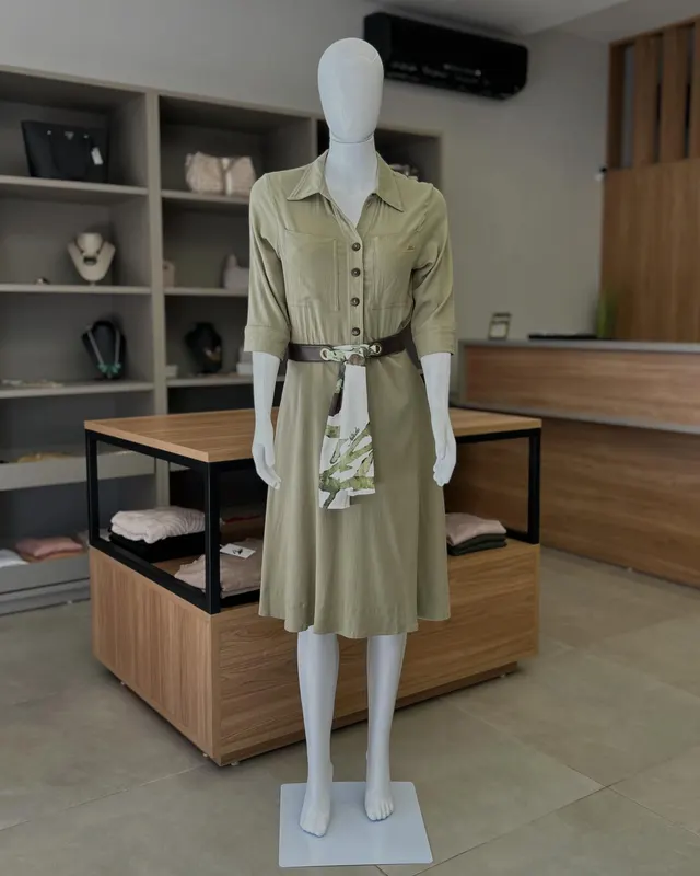 Vestido midi verde-oliva de botões com cinto, no manequim, dentro da loja